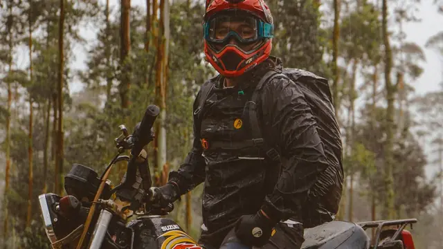 Motorista con casco y gafas junto a su moto en el bosque