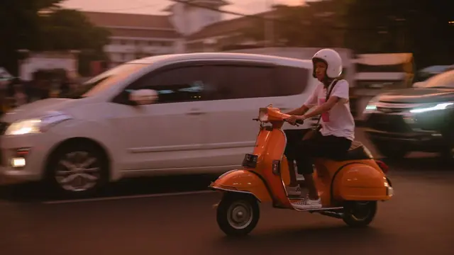 Motorista con casco jet en una Vespa naranja por la ciudad